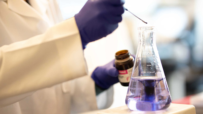 hand dropping something into flask in lab