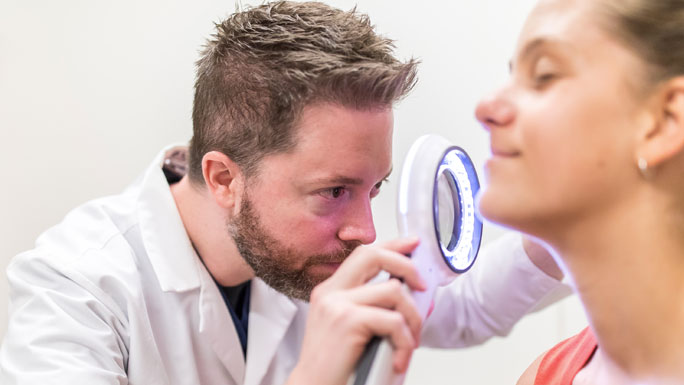John Fox, MD, looking at patient's skin