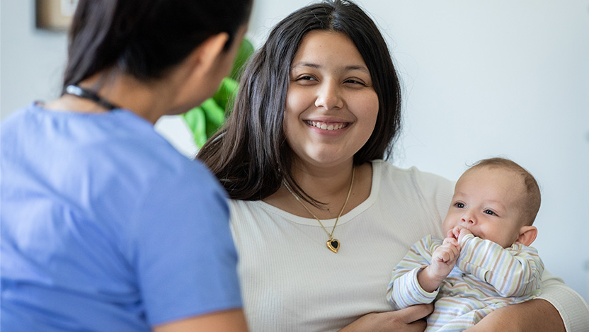 Image of parent holding her baby while talking to a nurse