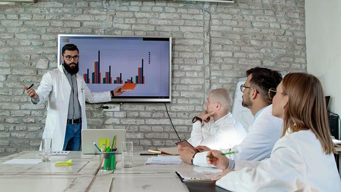 Physicians in lab coats watching a presentation in a conference room.