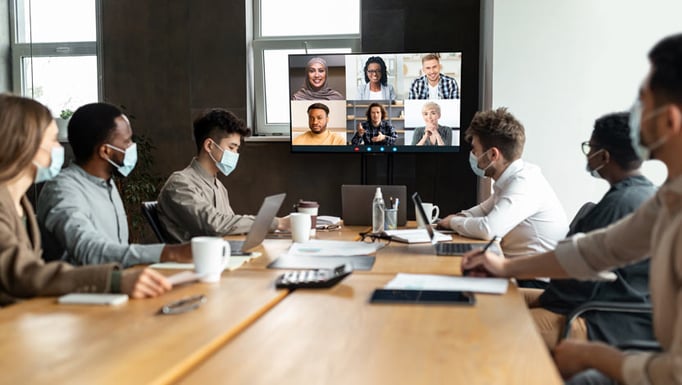 people around a table wearing masks, participating in a meeting with others online