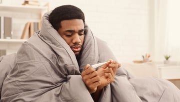 Person wrapped in blanket looking at thermometer