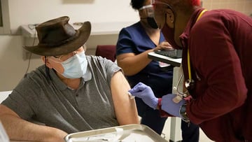 Man in a mask receiving a COVID vaccination injection from a female nurse