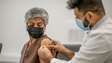 Masked nurse places bandaid on masked patient