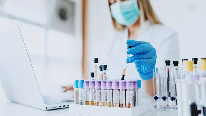 A lab assistant in rubber gloves holds a test tube with a blood sample.