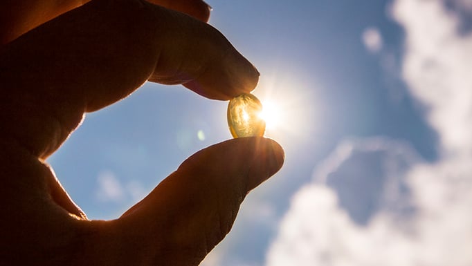 A hand holding up a pill up to the sun.