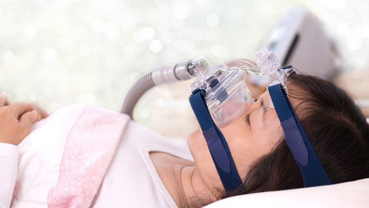 Happy and healthy senior woman sleeping deeply on her back with CPAP machine mask and hose.