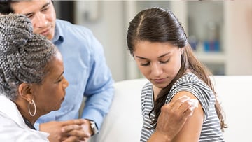 Father watching as doctor places bandage on teen