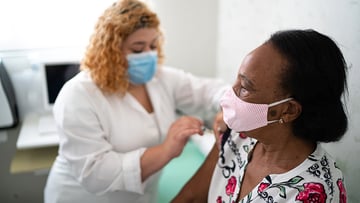 A masked nurse applying a vaccine to a masked patient