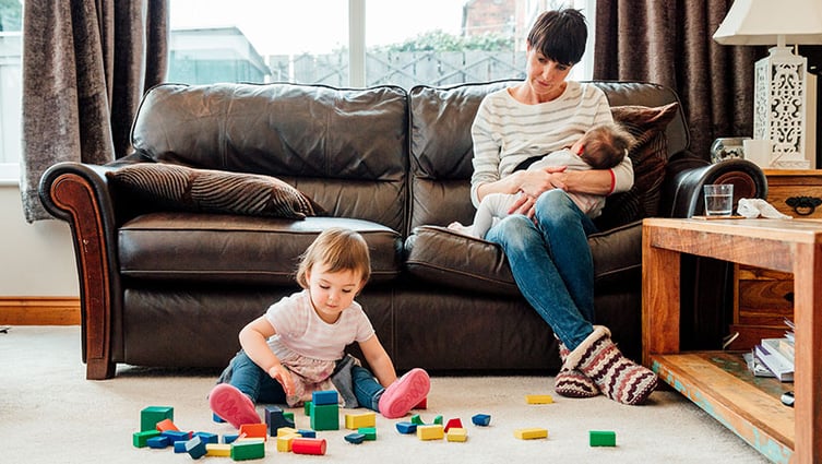 Mom breastfeeding infant with toddler playing nearby