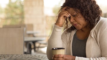 Woman with hand on her forehead while having coffee
