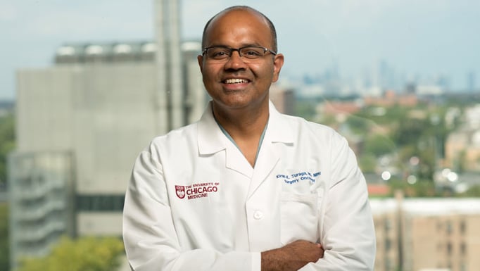 Kiran Turaga, MD, MPH, in front of window overlooking Chicago skyline from Center for Care and Discovery