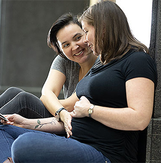 rei-lesbian-couple-sitting-hand-baby-bump-highlight-320x324