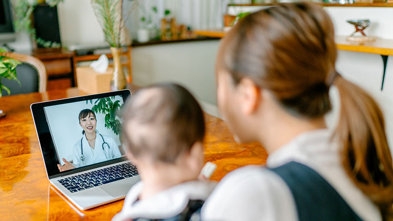 Woman holding a baby looking at a computer where she is chatting with a doctor