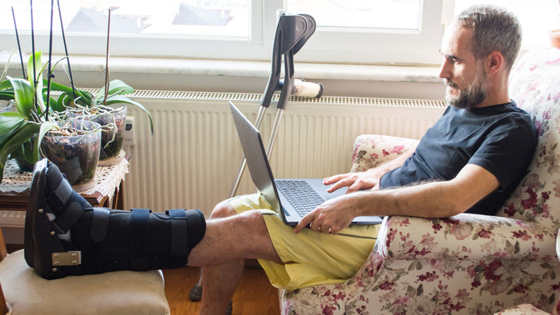man with foot brace viewing laptop