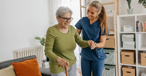 Female caregiver helping and supporting senior patient to walk at home, senior women is standing and holding walking cane