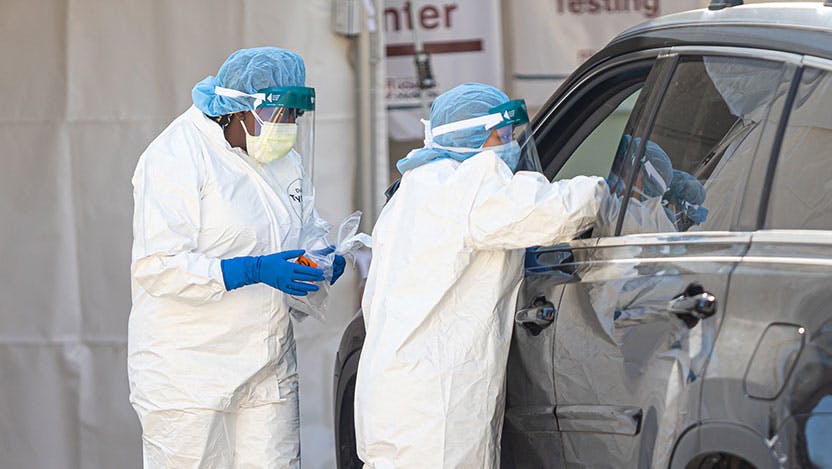 Healthcare workers in PPE testing patients in a car