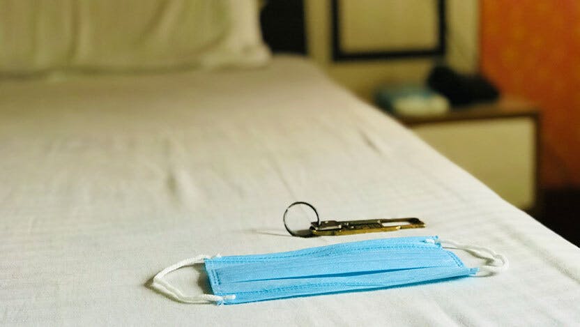 A mask on a hotel bed next to keys.