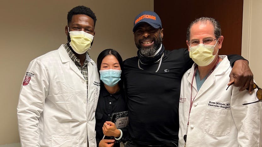 Leon Darby, a tall African-American man wearing his "#AorticMan" cap, poses with a few members of his care team: vascular surgery resident James Oyeniyi, MD, aortic nurse Julie Park, RN, and vascular surgeon Ross Milner, MD