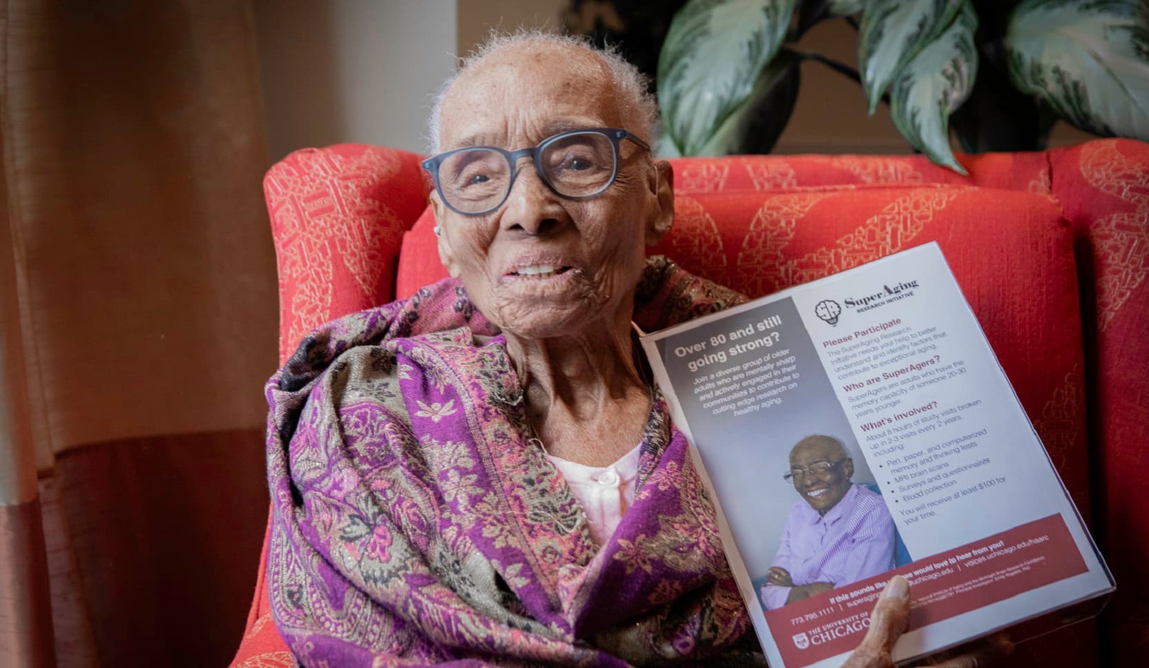 SuperAger Edith Renfrow Smith, 110, a petite Black woman, holds a flyer for the SuperAging Research Initiative that features a photo of her.
