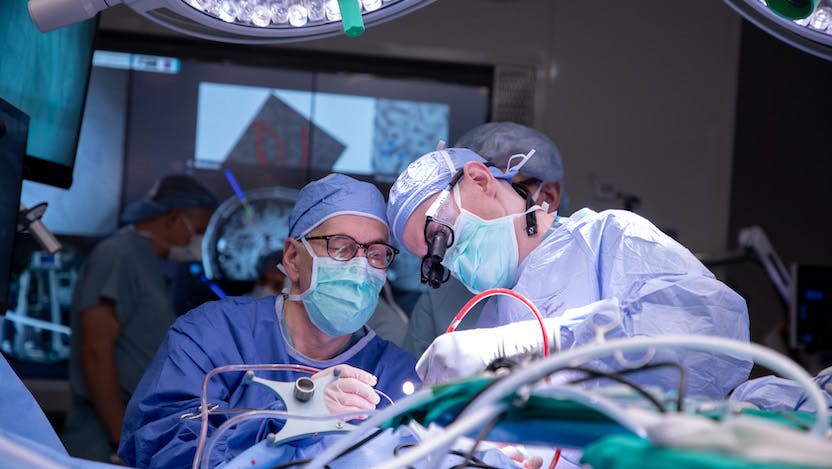 Peter Warnke, MD, and a colleague perform a delicate neurosurgery in the high-tech OR. Relevant images of the patient's brain are displayed on the screens to guide the procedure.