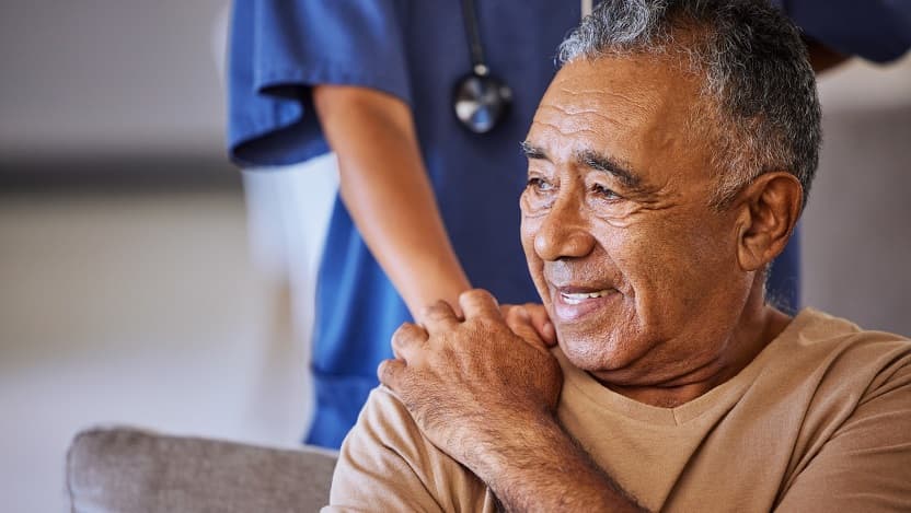 An elderly man holds the hand of a healthcare worker over his shoulder