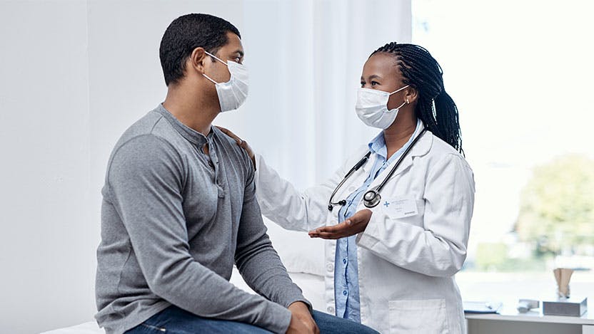 Masked doctor speaking with masked patient in clinic room