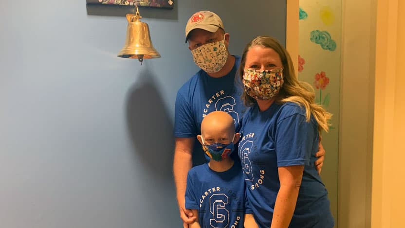 Carter with his parents Randy and Jennifer Fortin, standing next to the bell
