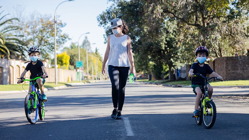Masked mom walking with masked kids on bikes