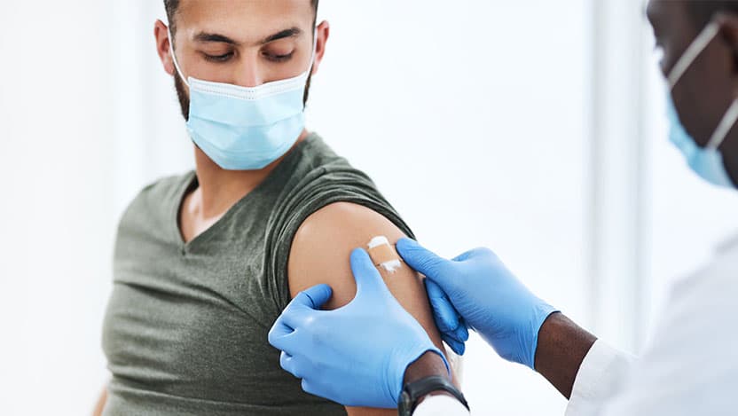 Masked provider places bandaid on masked patient's arm after shot