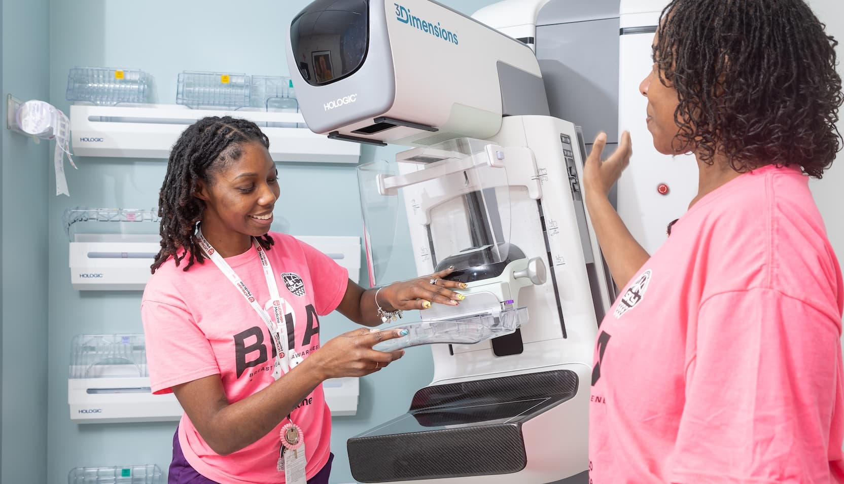 Two workers in pink shirts with mammogram machine