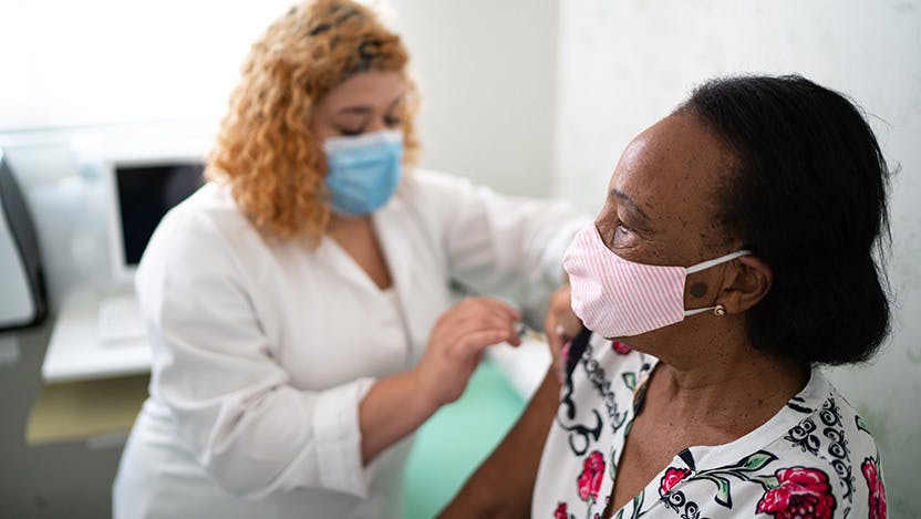A masked nurse applying a vaccine to a masked patient's arm.