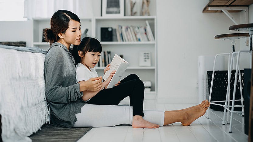 Mother sitting on bedroom floor reading with child
