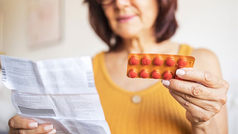 Woman holding hormone therapy pills and reading instructions