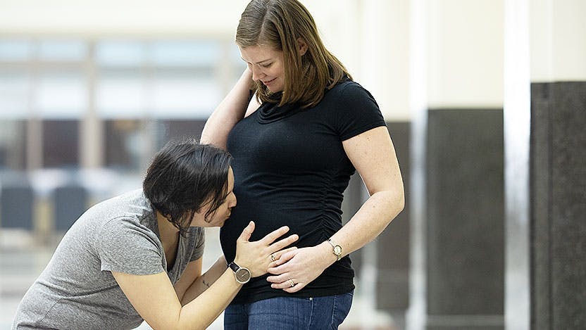 A woman kisses her partner's baby bump.