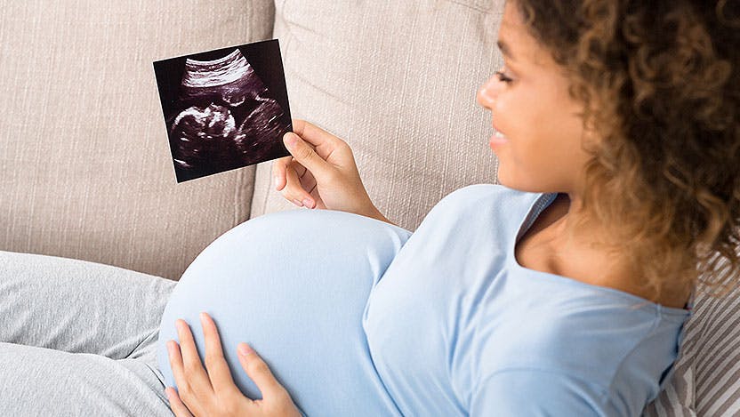 Pregnant mom resting on couch and smiling at sonogram
