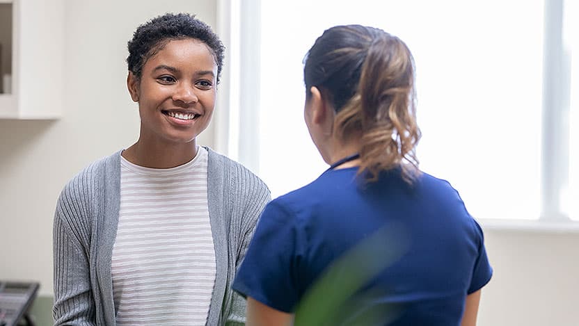 Smiling female patient speaking with female nurse in exam room