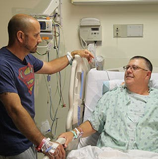 Kidney transplant patient Stewart Botsford (in bed) and his donor, Justin Maduena, visit with each other in Mitchell Hospital after their surgeries two days earlier.
