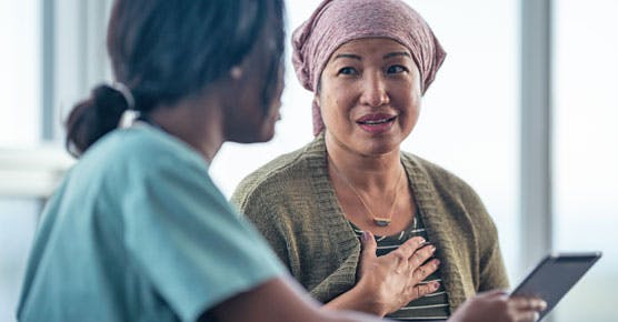 Asian female cancer patient wearing headscarf, talking to female nurse or doctor