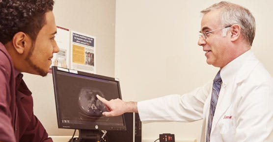 Medical oncologist Kenneth Cohen, MD, pointing to a computer and talking with a patient