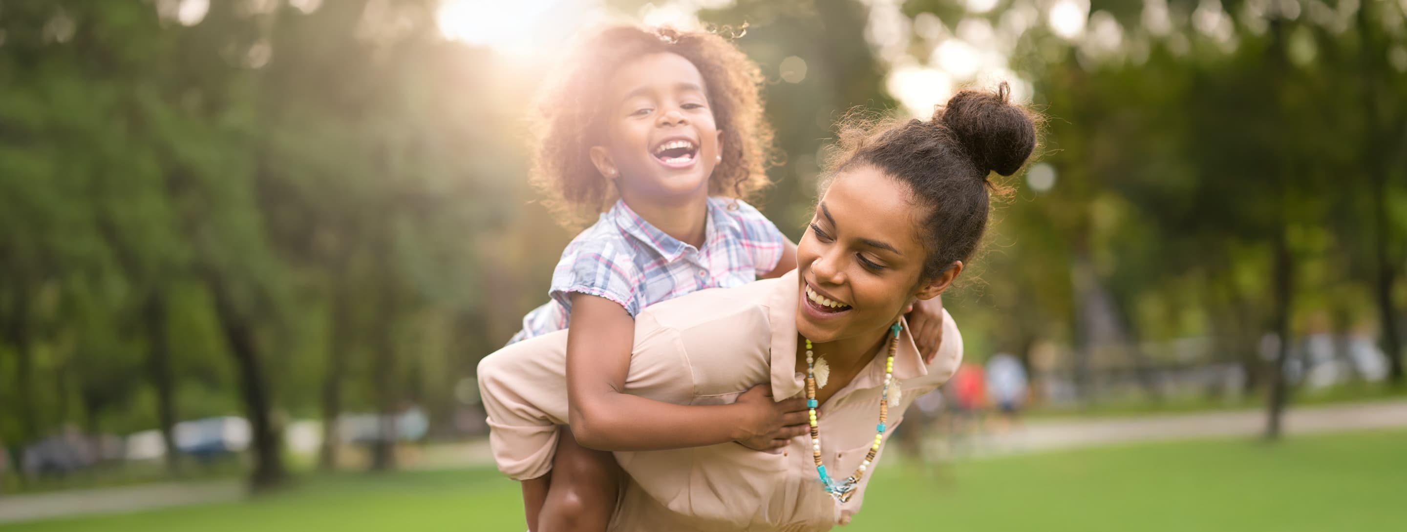 Mom giving boy piggy back ride in park